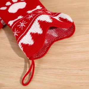 Red knit Christmas bone stocking with white paw prints and snowflakes on a wood background