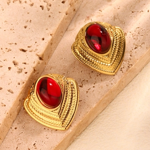 Detail of vintage heart earrings with deep red stone on beige sandstone background