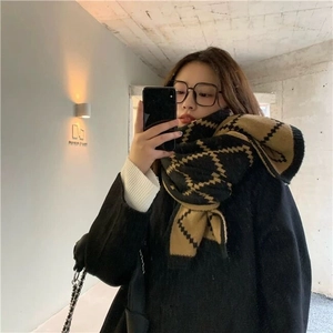 Detail of thick black and brown diamond pattern knit scarf worn in casual indoor setting
