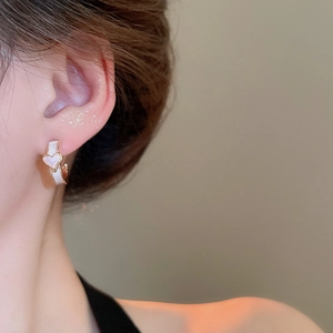 Gros plan d'une boucle d'oreille dorée en C avec détail de cœur blanc sur modèle