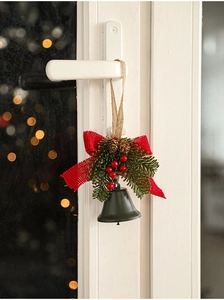 Green metal bell with pine cones and red berries hanging on a white door handle