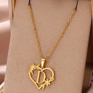Dettaglio collana cuore dorato con lettera D e motivi floreali su scatola di velluto