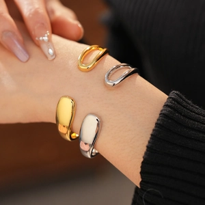 Detailed view of minimalist gold and silver teardrop open bangles worn by a model