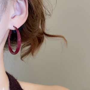 Close-up of model wearing large burgundy enamel geometric hoop earrings with a glossy finish