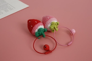 Close-up of handmade crochet strawberry charms in red and pink on a soft pink surface