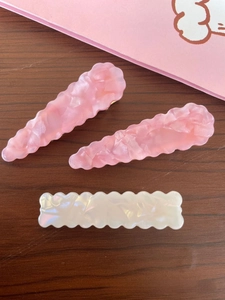 Detail of pink and pearl white acetate hair clips with wavy edges on dark wood surface