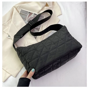 Detail of black quilted shoulder bag with wide adjustable strap on a minimalist background