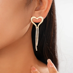 Close-up of golden heart earrings with dangling rhinestone tassels worn by a model
