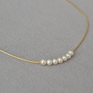 Detail of 7 round white pearls on a minimalist gold chain necklace with a gray backdrop