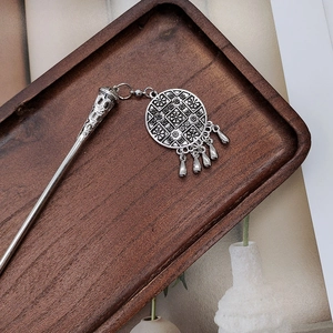 Detail of vintage silver tassel hairpin with retro flower pattern on a wooden tray