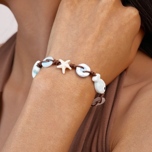 Close-up of woven bracelet featuring ceramic starfish, flower and fish beads on wrist