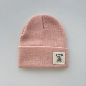 Detailed close-up of a pink knit beanie featuring a cute bear patch and soft texture