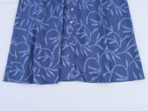 Détail d'une robe en jean bleue avec texture jacquard feuille et boutons blancs