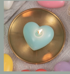 Lit mint green heart scented candle on a gold tray with white knitted background
