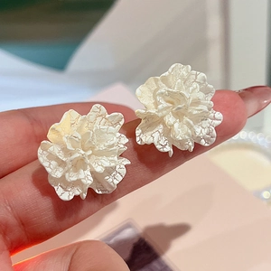 Close-up of white floral stud earrings with unique crackle texture and metal finish