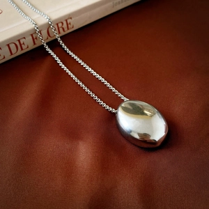 Detailed view of polished silver oval pebble pendant on long geometric sweater chain