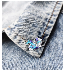 Enamel astronaut riding whale brooch pinned on a blue denim jacket collar