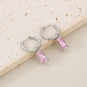 Détail de boucles d'oreilles argentées avec zircon rose rectangulaire et texture martelée