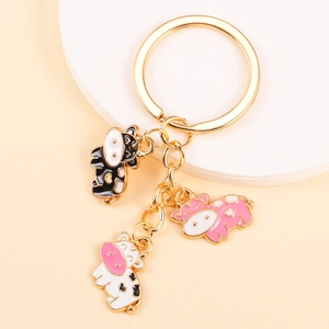 Cute gold metal keychain with three enamel cow charms in black pink and white spots