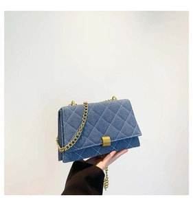 Detail of denim quilted crossbody bag featuring gold chain strap and metal buckle