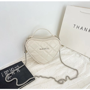 Dettaglio di borsa trapuntata a cuore color crema con logo in metallo argento su pizzo
