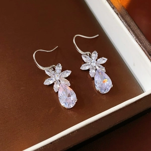 Macro shot of silver-tone teardrop zircon earrings with floral petal accents in a gift box