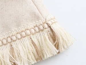Détail macro du tissu en lin beige avec bordure à franges dorées et texture tissée