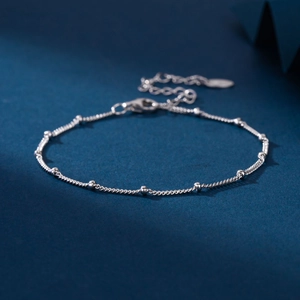 Macro detail of silver beaded rope chain bracelet with adjustable link and pendant on blue