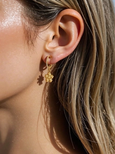 Close-up of gold-plated hoop earrings with a sparkling zircon flower pendant on a model