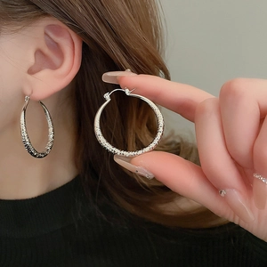 Detail of silver textured hoop earrings with a metallic grooved surface on model