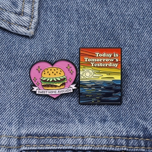Detailed close-up of cartoon heart burger and sunset scenery enamel pins on denim jacket