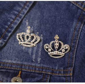Close-up of crown brooches with rhinestones and pearls on a blue denim jacket pocket