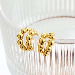 Detail view of gold bubble bead C-shaped earrings hanging on a textured glass edge