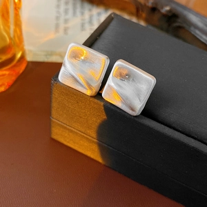 Detail view of square marble texture earrings with silver-white finish on a black box