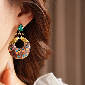 Close-up of vintage peacock earrings with green gemstones and detailed enamel feathers