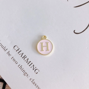 Close-up of pink enamel round charm with golden letter H for DIY jewelry making