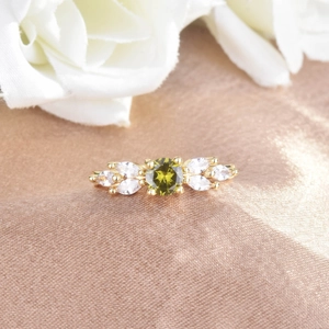 Detail shot of a golden ring featuring an olive green center zircon and clear side stones