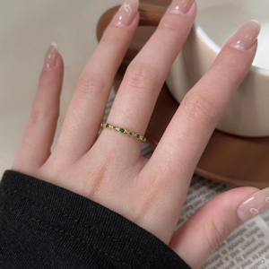 Detailed view of an 18K gold ring featuring marquise-shaped green gemstones on a hand