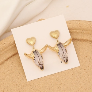 Vintage bull skull drop earrings with gold heart studs on elegant silk background