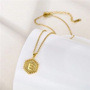 Detail of gold-plated hexagonal pendant with letter E on a minimalist thin chain