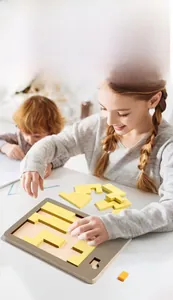 Zwei Kinder konzentrieren sich auf ein gelbes Holzpuzzle zur Logikförderung
