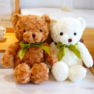 Pair of cute fluffy brown and white plush teddy bears with green ribbons on a wooden desk.