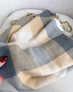 Close-up of soft plaid scarf fabric showing gray and cream textures with fringe detail