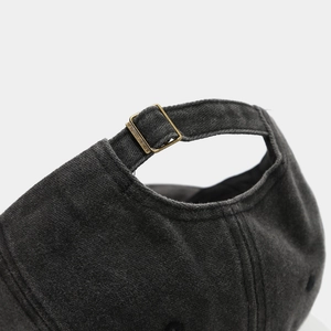 Close-up of adjustable bronze metal buckle on dark grey washed cotton baseball cap