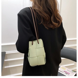 Close-up of light green hand-woven bucket bag featuring soft leather and thin brown strap