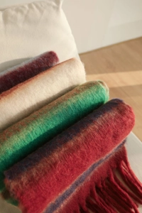 Close-up of stacked thick knit striped scarves with fringe in assorted autumn colors