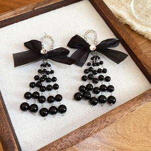 Detail of silver bow earrings with black bead tassels and sparkling crystals on fabric