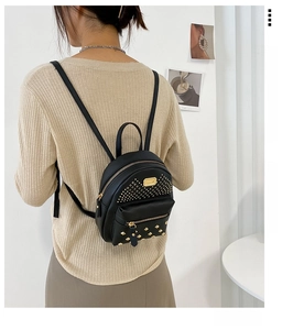 Detailed view of women's mini black backpack with golden rivets worn by model