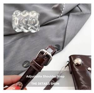 Detail of adjustable dark brown patent leather strap with silver metal buckle on bag