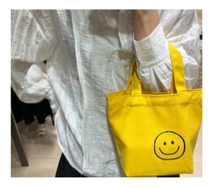 Close-up of bright yellow canvas mini tote bag with a black smiley face pattern